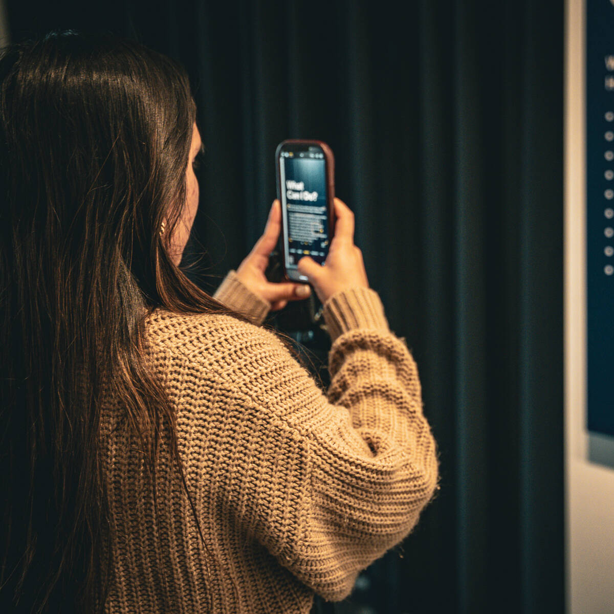 Over the shoulder of a girl taking a photo of a banner titled "What Can I Do?"